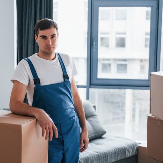 Young male mover in blue uniform works indoors in the room.